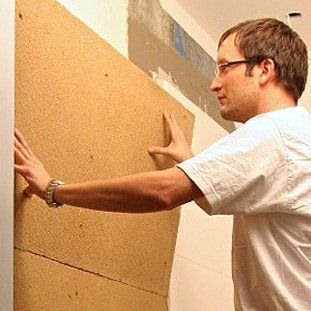 Ein Mann hält ein Stück Holz an einer Wand fest.