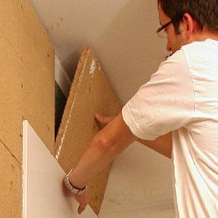 Ein Mann hält ein Stück Holz an einer Wand fest.