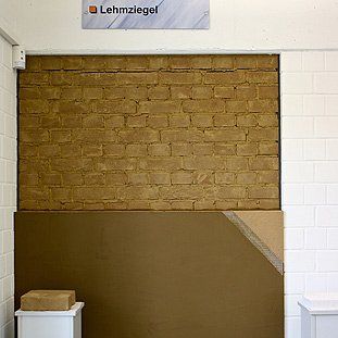 Eine Backsteinmauer mit einem Schild darüber, auf dem Lehmziegel steht.