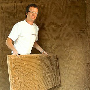 Ein Mann hält ein Stück Holz vor einer Wand.