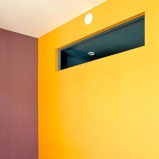 Eine gelbe Wand mit einem Fenster in der Ecke eines Zimmers.