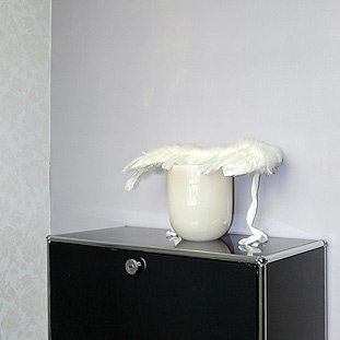 Auf einer schwarzen Kommode steht eine Vase mit weißen Federn darauf.