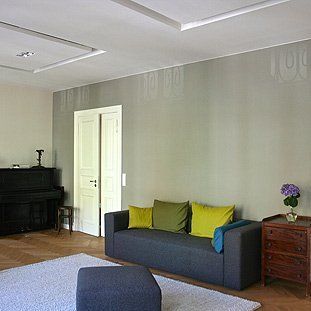Ein Wohnzimmer mit Couch, Ottomane und Klavier.