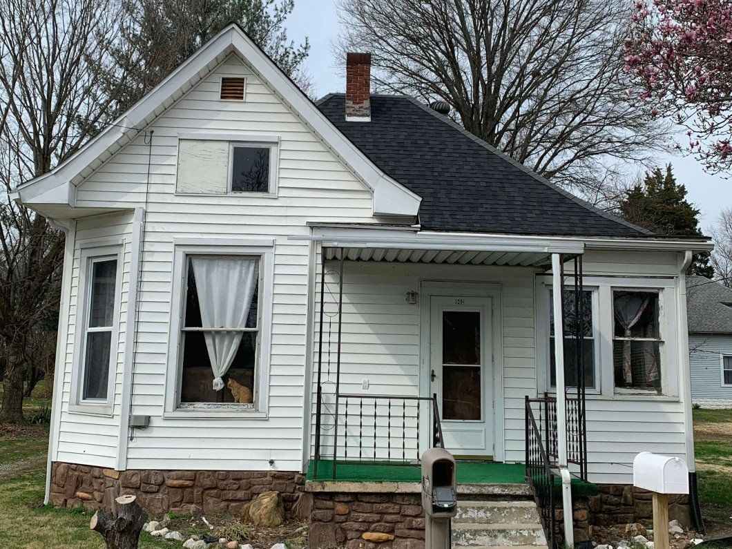 A small white house with a porch and a mailbox in front of it.
