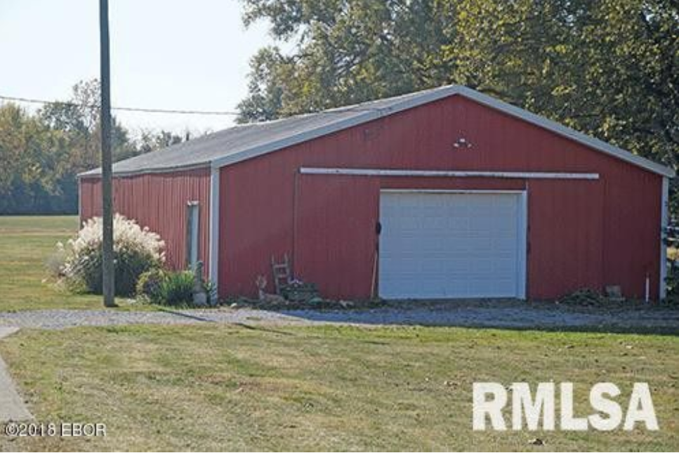 A large red barn with a white garage door is for sale.