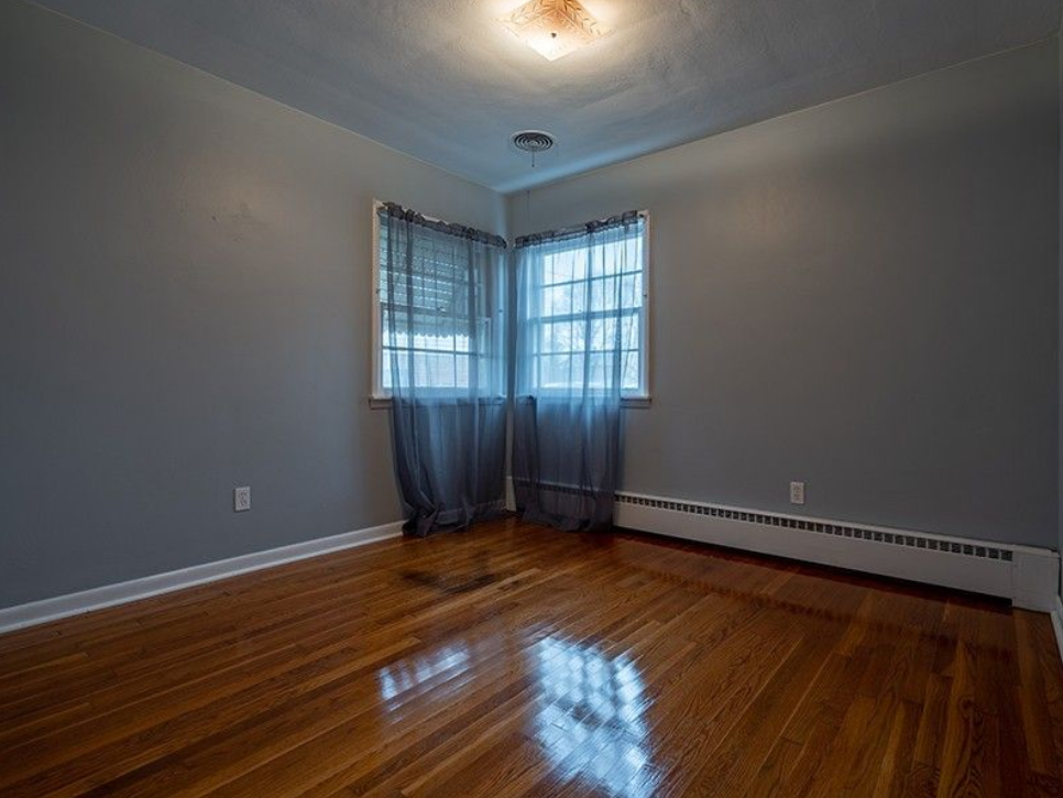An empty room with hardwood floors and two windows.