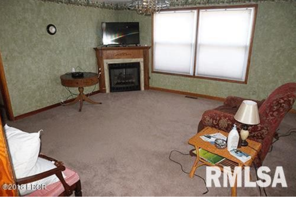 A living room with a fireplace , chairs , table and television.
