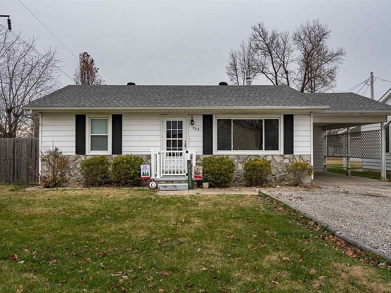 A white house with a gray roof and black shutters is for sale.