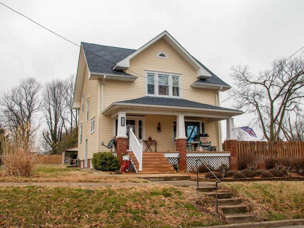 A large yellow house with stairs leading up to the front porch.