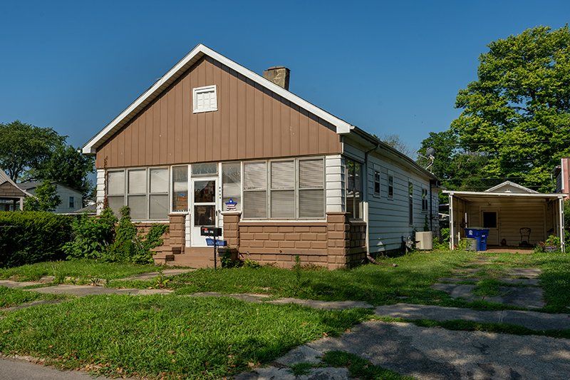 A small house with a brown siding and a white roof is sitting on a lush green lawn.