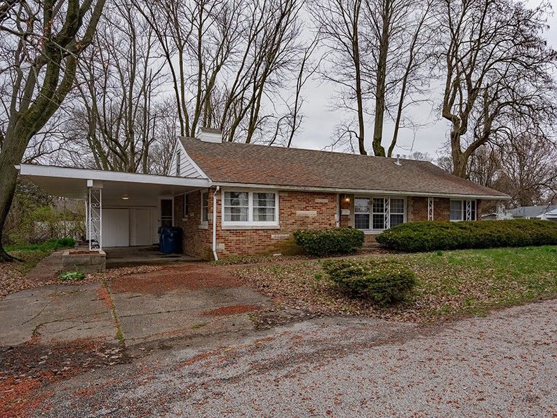 A brick house with a covered porch and trees in the background.