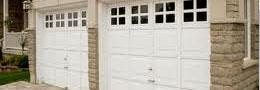A couple of white garage doors with windows on a brick building.