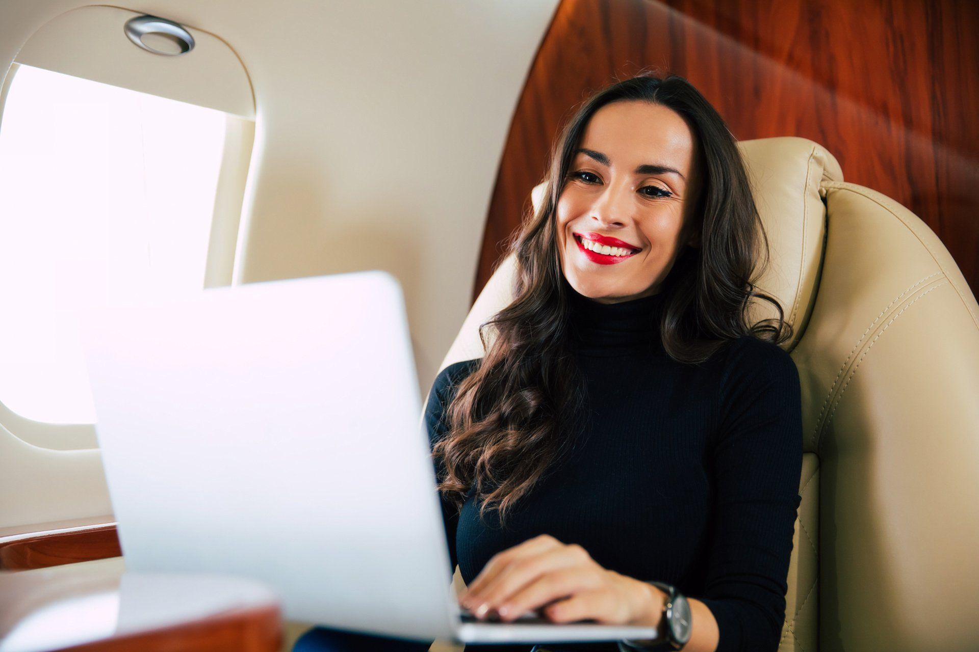 A woman is sitting on an airplane using a laptop computer.