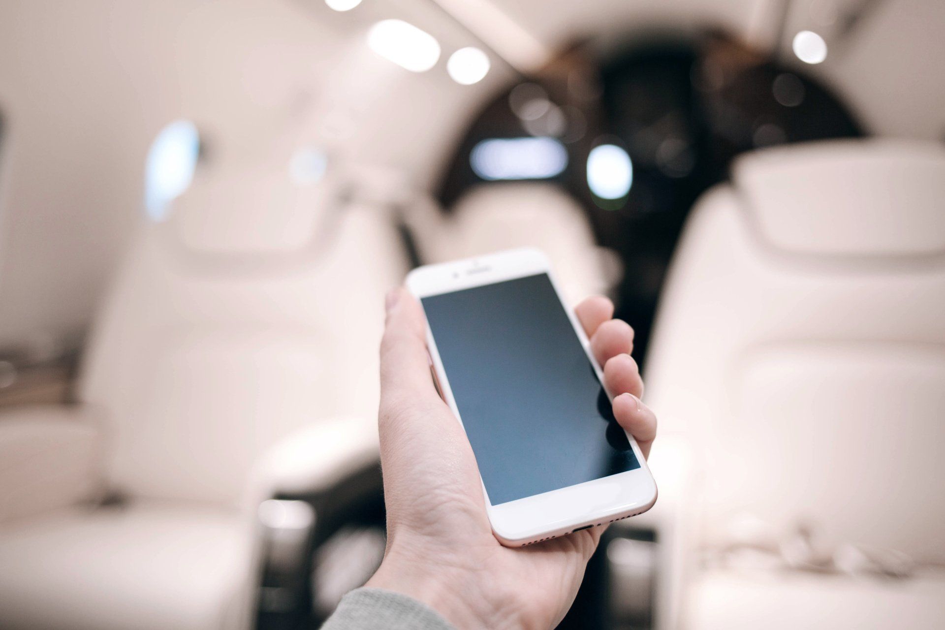 A person is holding a cell phone in their hand in an airplane.