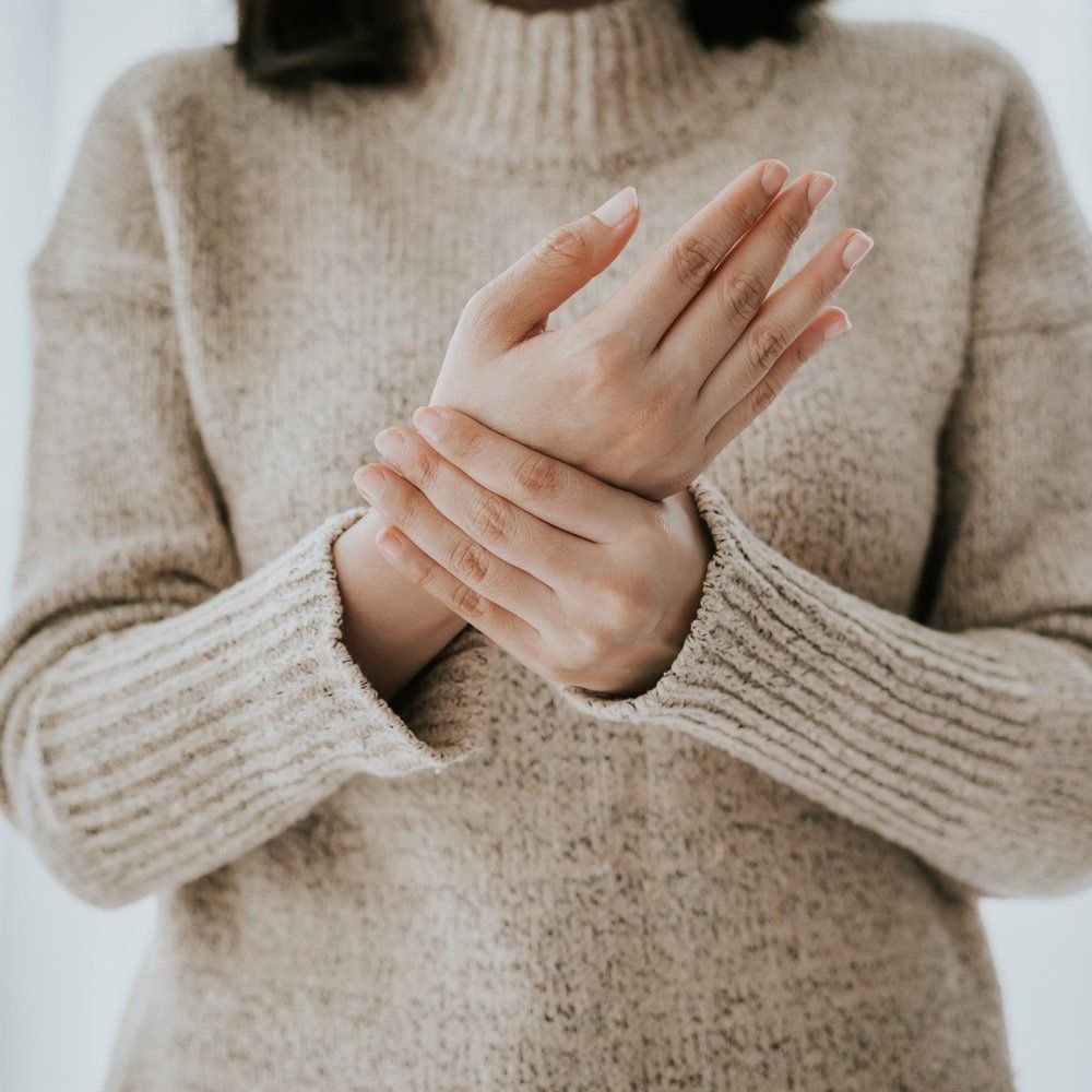Person holding their wrists, wearing a beige turtleneck sweater.
