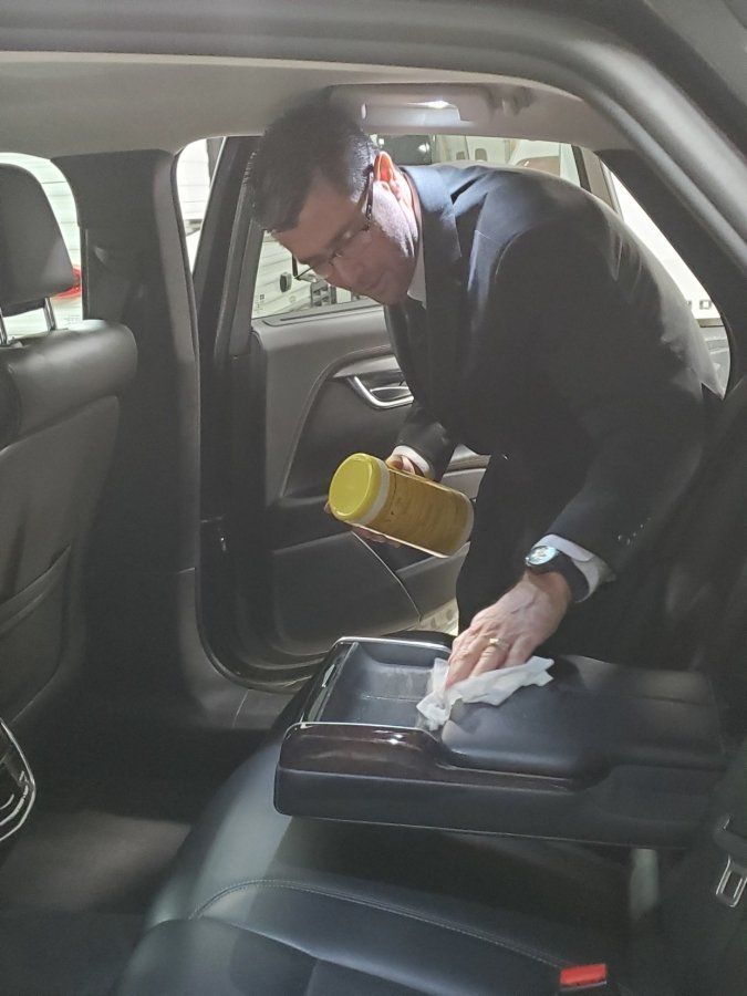 A man in a suit is cleaning an disenfecting the inside of an Iowa City sedan with Xquisite Limo