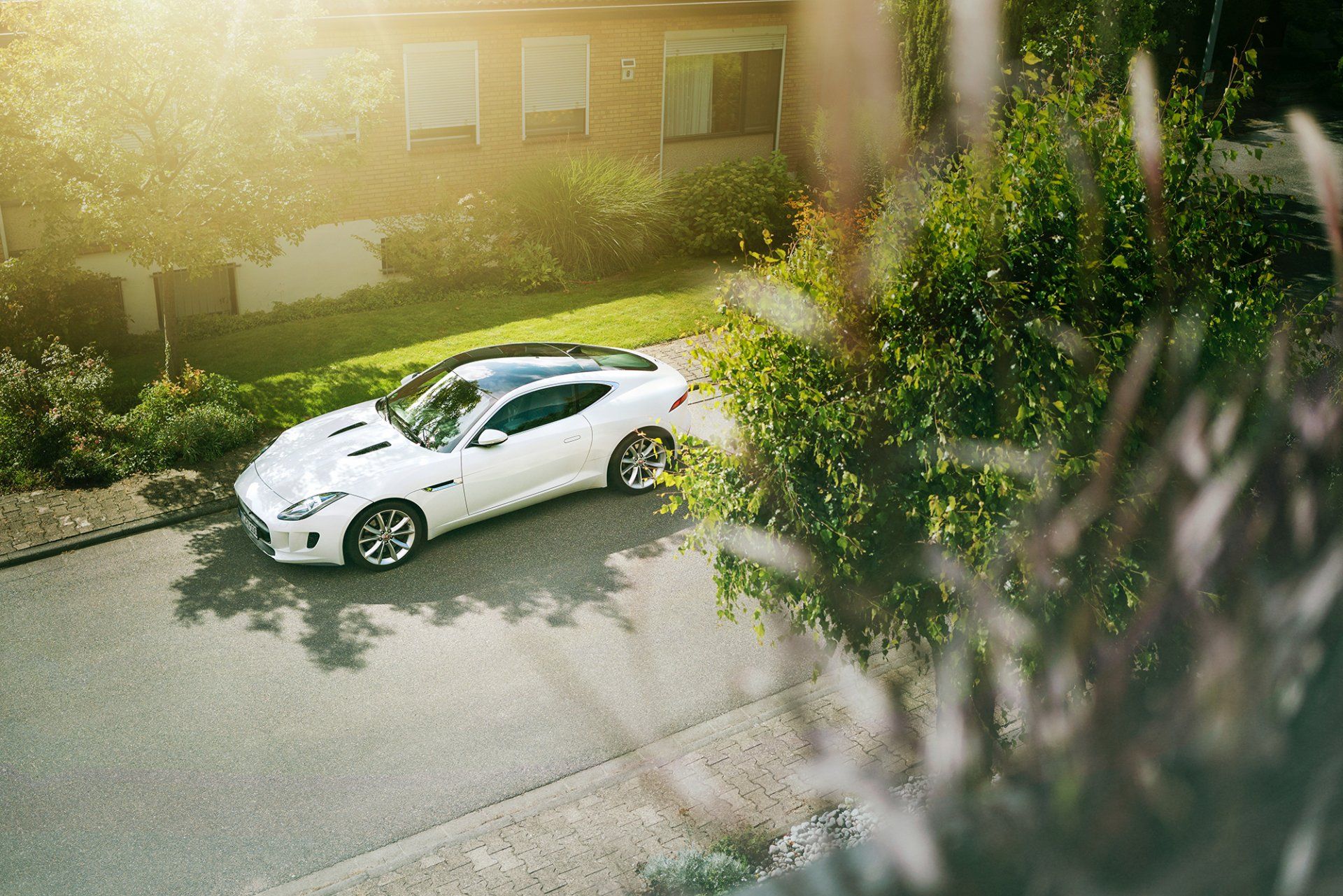 A white sports car is parked on the side of the road in front of a house.