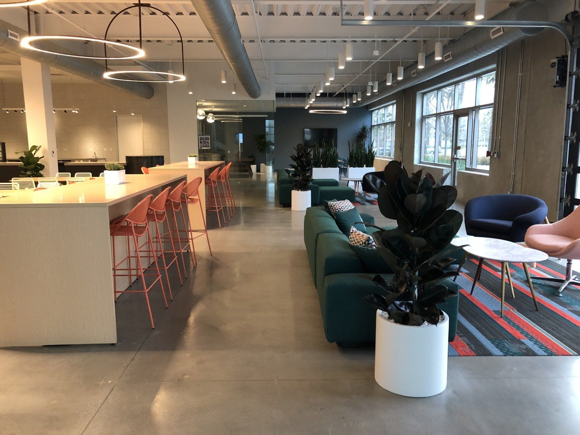 Modern office interior with seating area, long counter with bar stools, and plants.