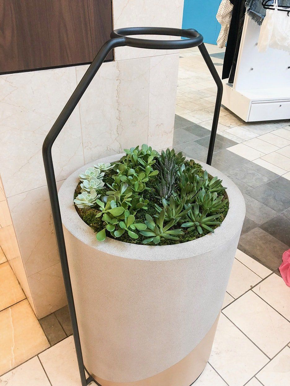 A cylindrical concrete planter with greenery, supported by a black metal frame.