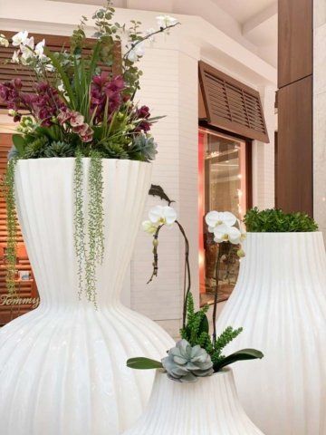 White sculpted planters filled with various flowers and greenery.