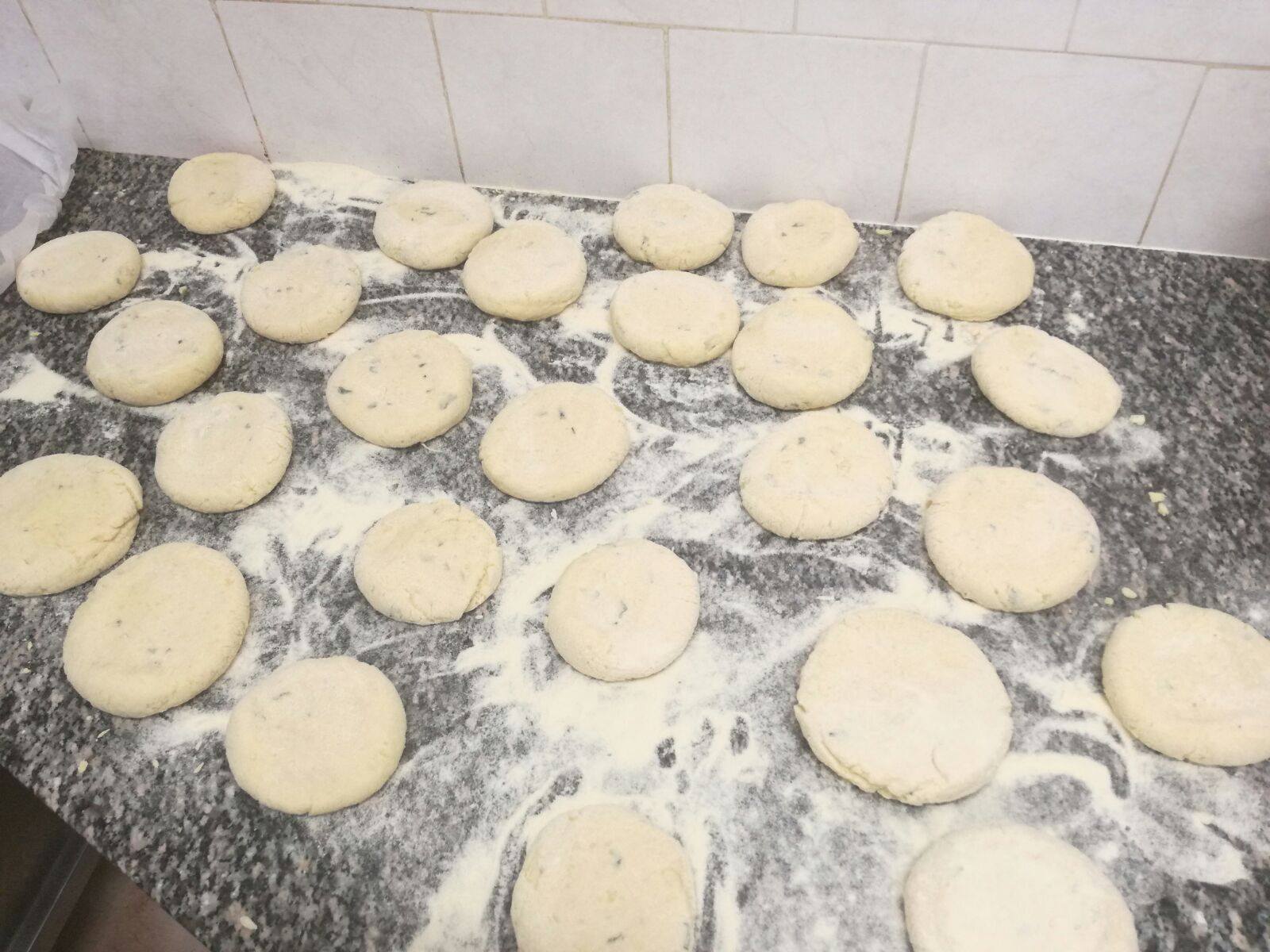 Numerose palline rotonde di pasta cruda sono disposte su un piano di lavoro cosparso di farina bianca e macchie grigio scuro.