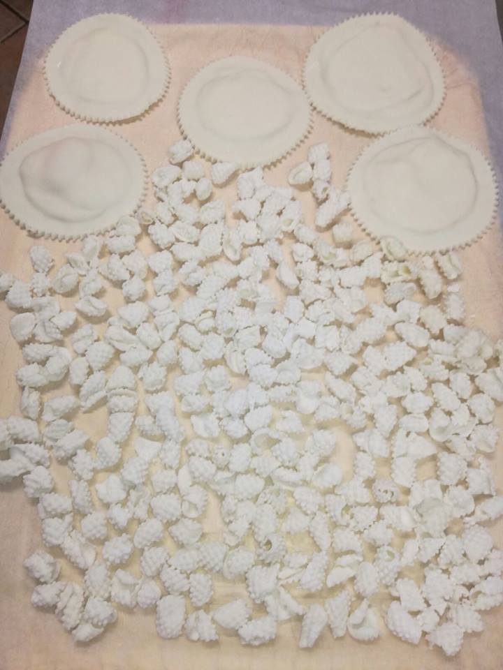 Quattro ravioli rotondi e sigillati e tanti piccoli gnocchi infarinati disposti su una superficie chiara ad asciugare.