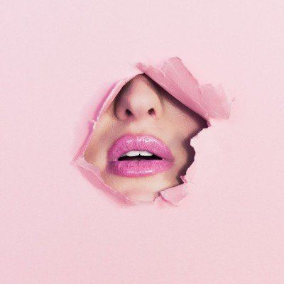 Pink lips and nose peeking through a torn pink paper background