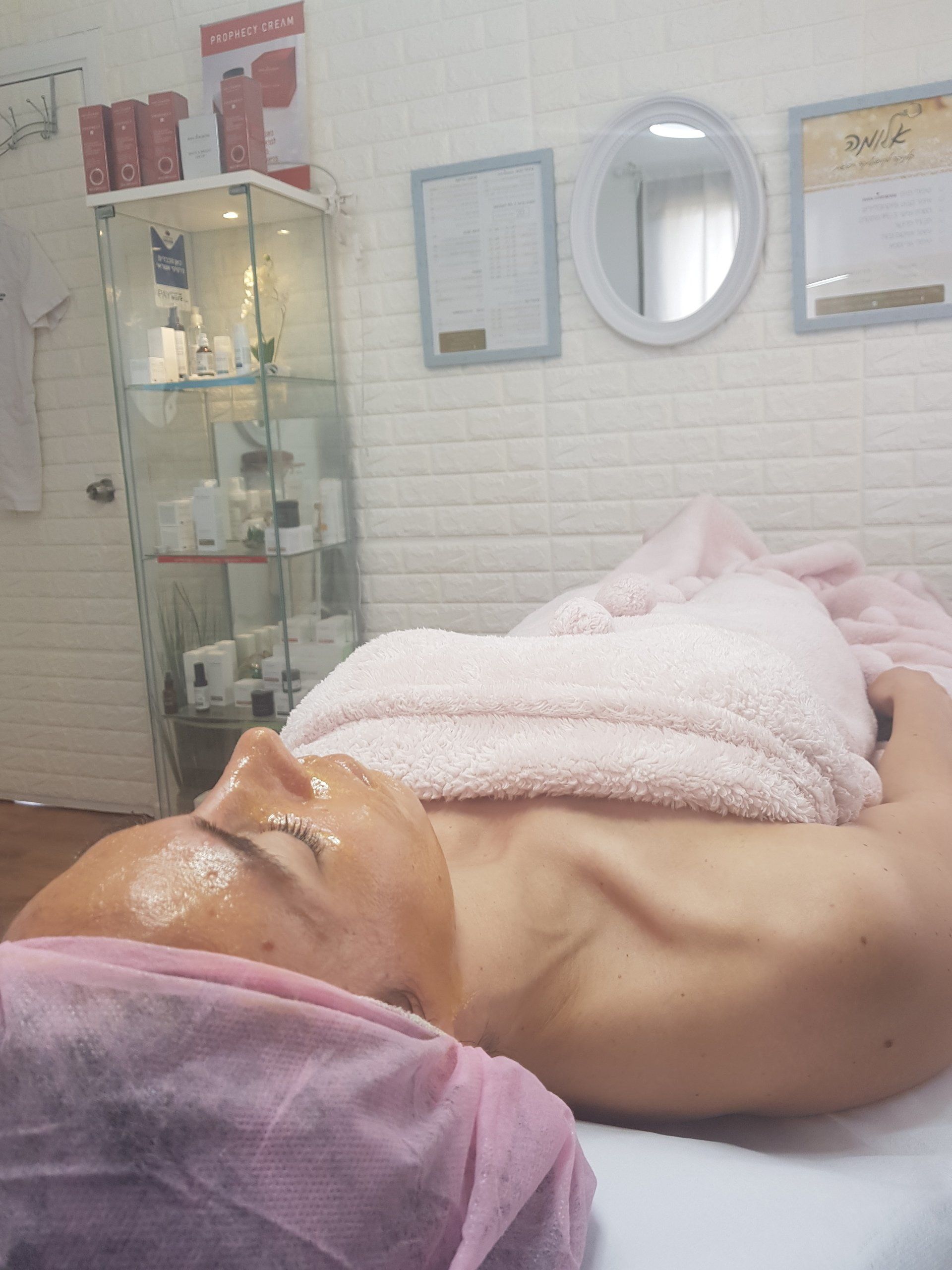 Person lying on a spa bed with face mask and towel in a treatment room