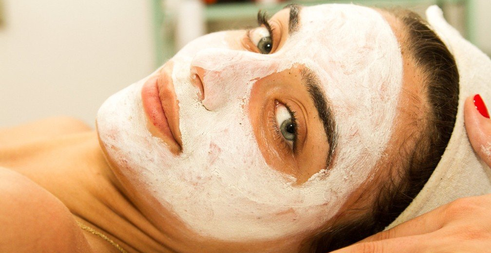 Person lying down with a white facial mask, resting on a towel