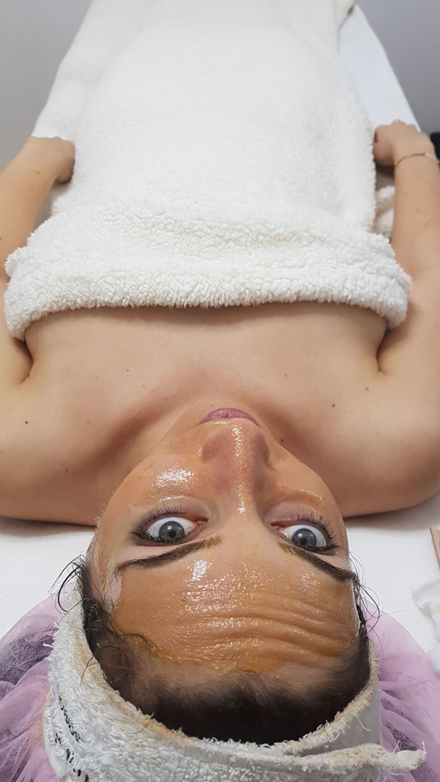Person lying on a massage table with a towel and white blanket, face up with eye mask and head wrap