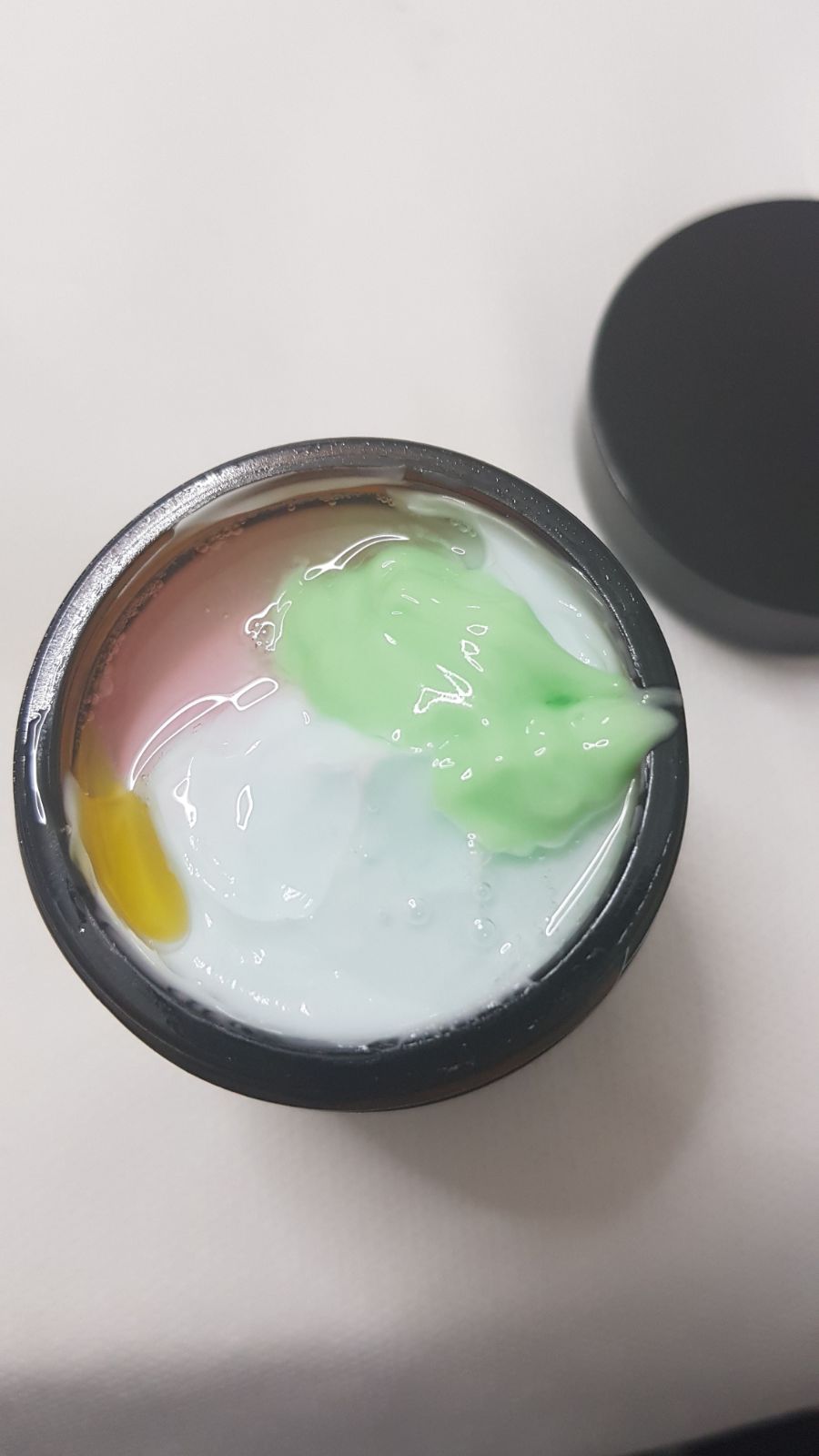 Open jar of colorful cream or paint with pink, green, yellow, and white swirls.