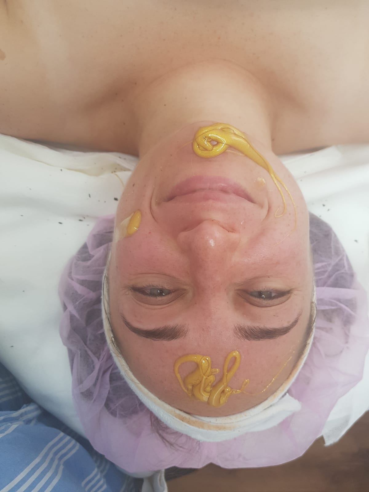 Person lying on a bed with a towel cap and yellow face mask, smiling gently.