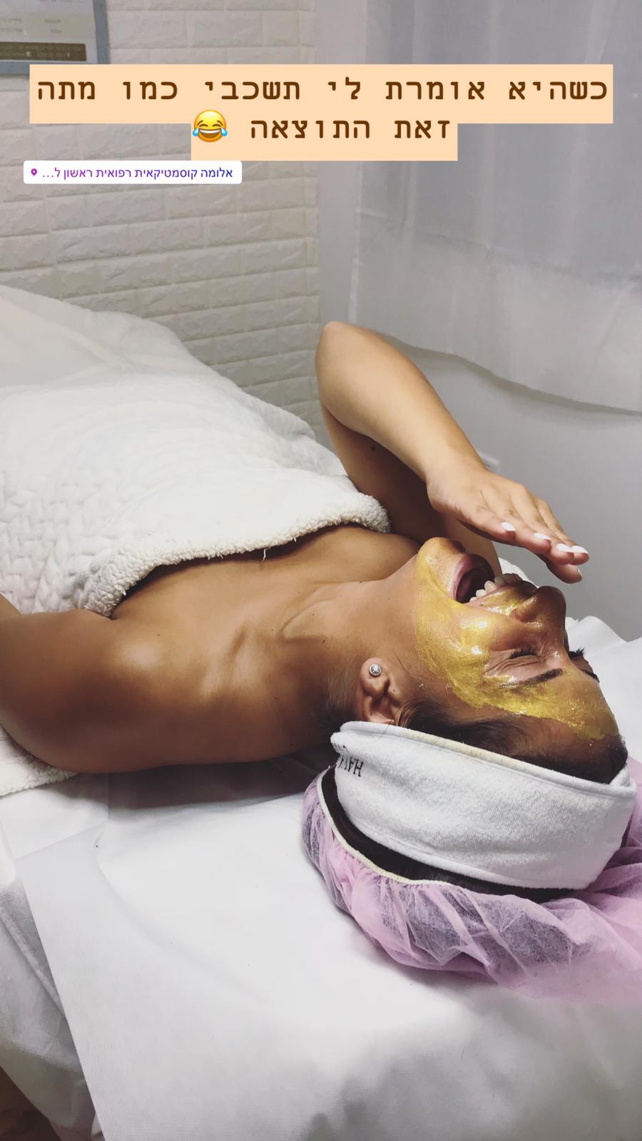 Person lying on a treatment bed with a gold facial mask and towel, in a spa/clinic setting.