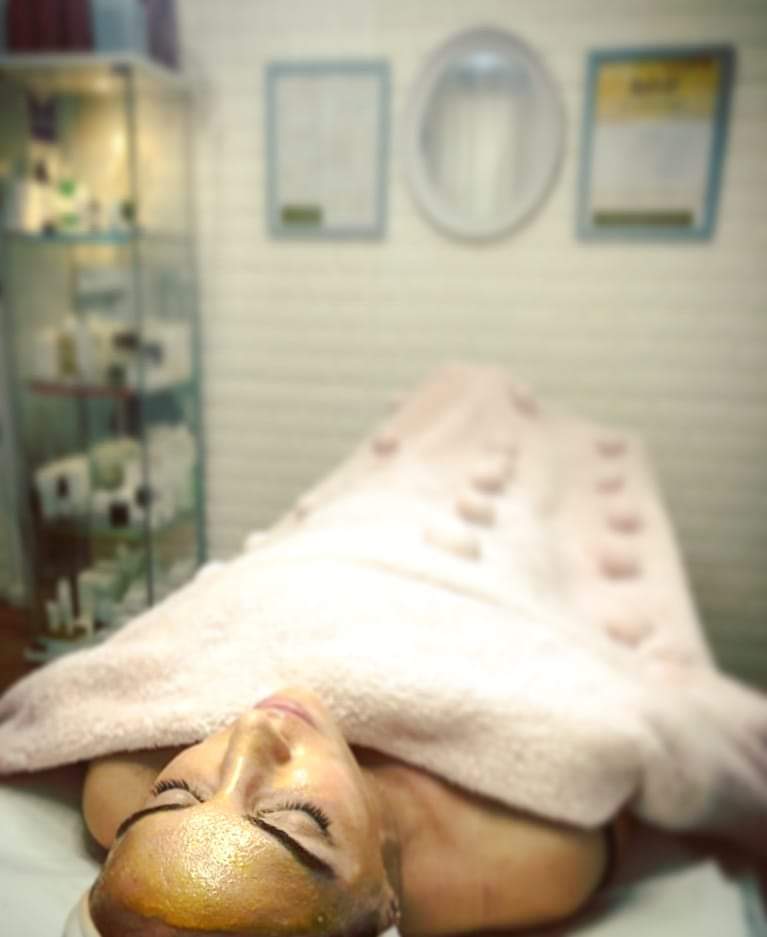 Woman lying on a spa table covered with a pink towel in a softly lit treatment room