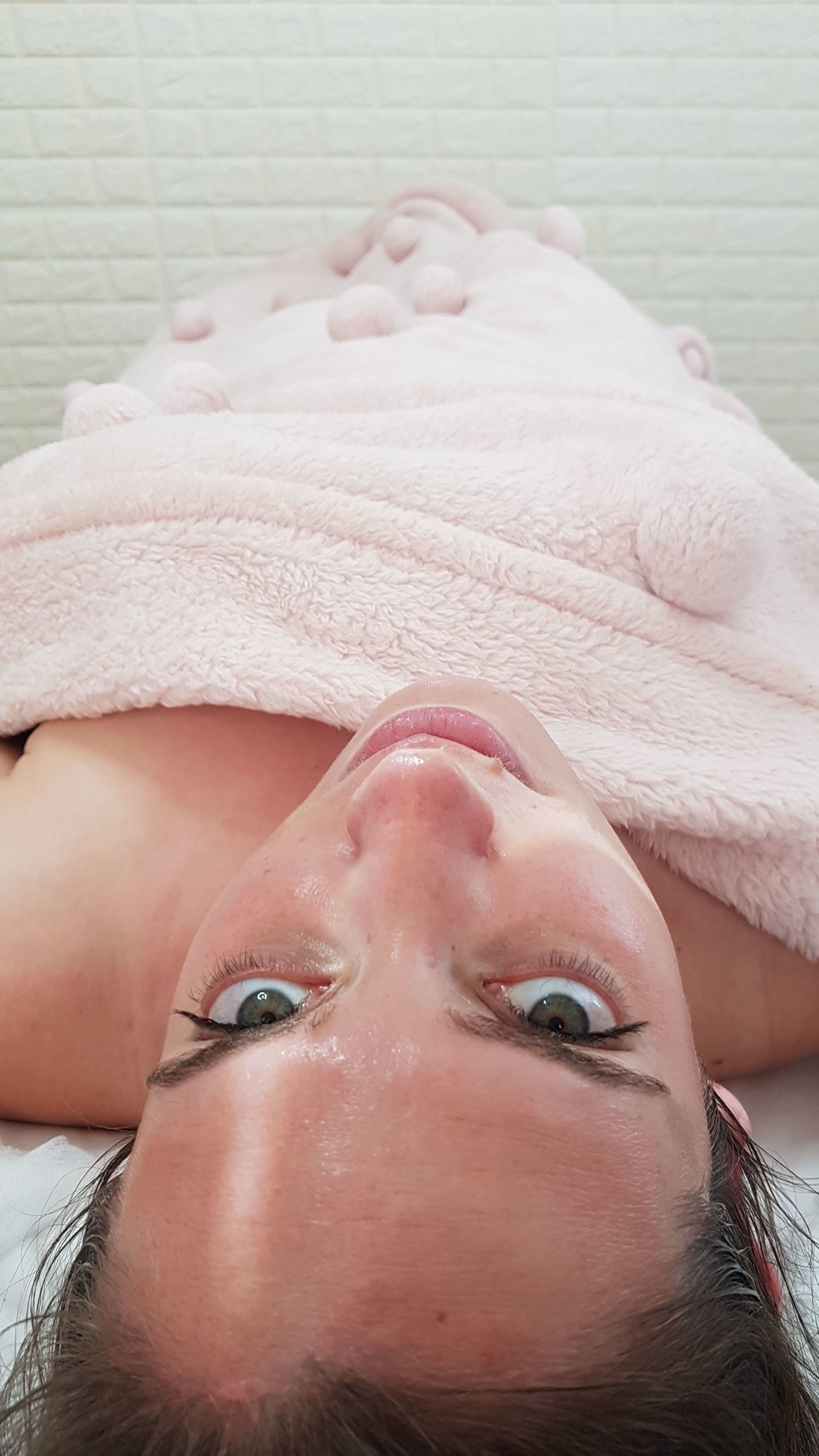 Person lying upside down, wrapped in a pink towel, looking at the camera.
