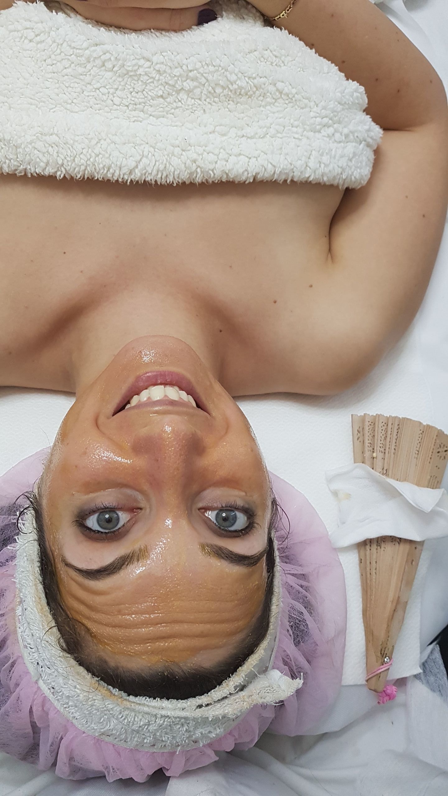Woman in a pink shower cap, smiling while lying on a spa treatment bed with a towel over her chest