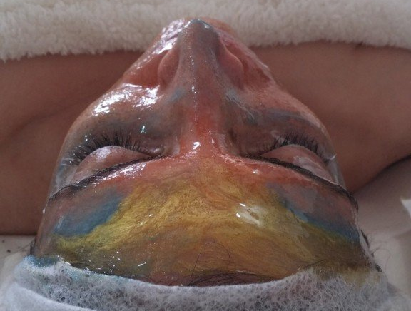Upside-down painted face with rainbow colors across the forehead and cheeks, eyes closed.
