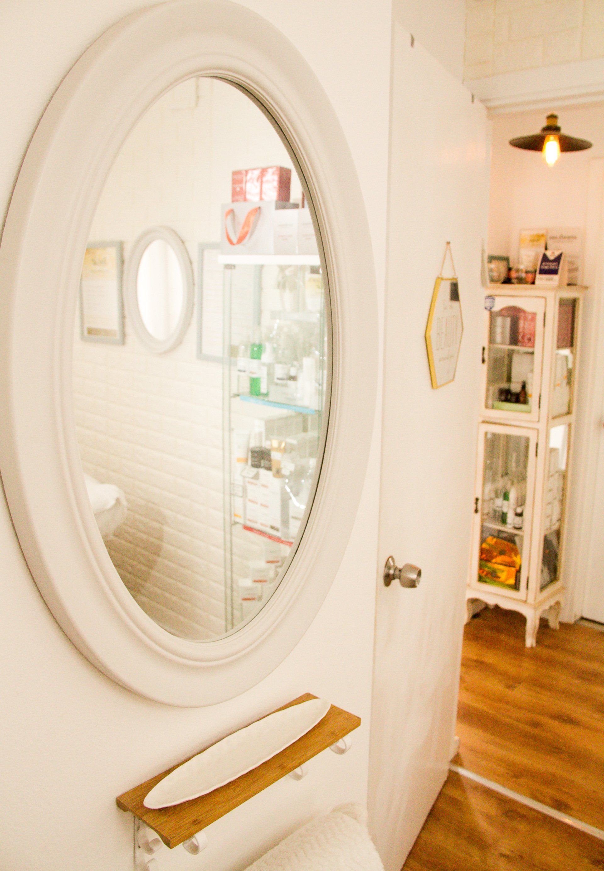 Bright hallway with an oval mirror, small shelf, and white door opening to a sunlit room with wood floors