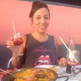 Smiling person holding a drink at a table with pizza, in a warm-lit restaurant.
