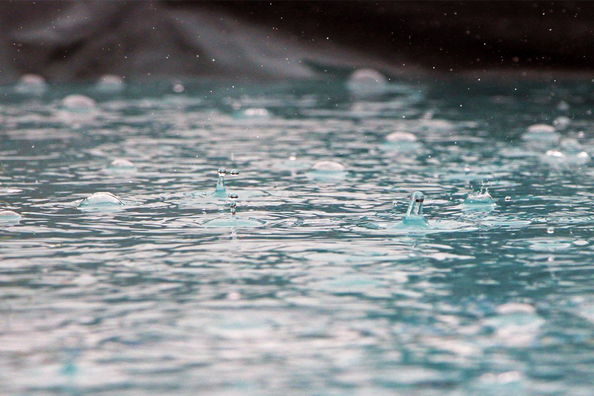 A close up of rain drops falling into a pool of water.