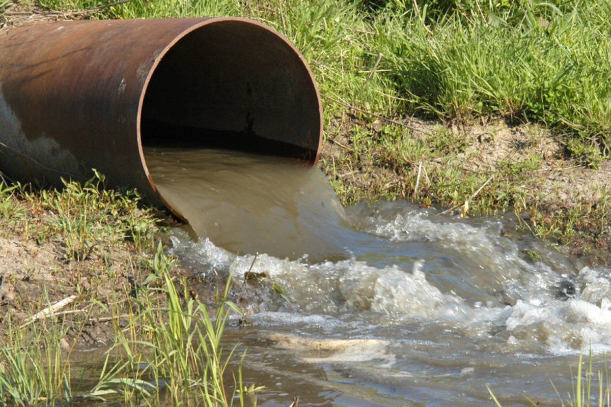 A rusty pipe is pouring water into a stream.