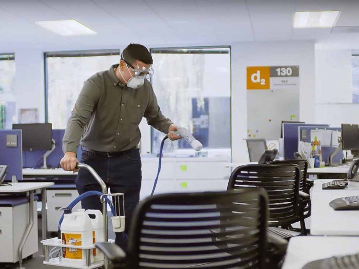 A man wearing a mask is disinfecting chairs in an office.
