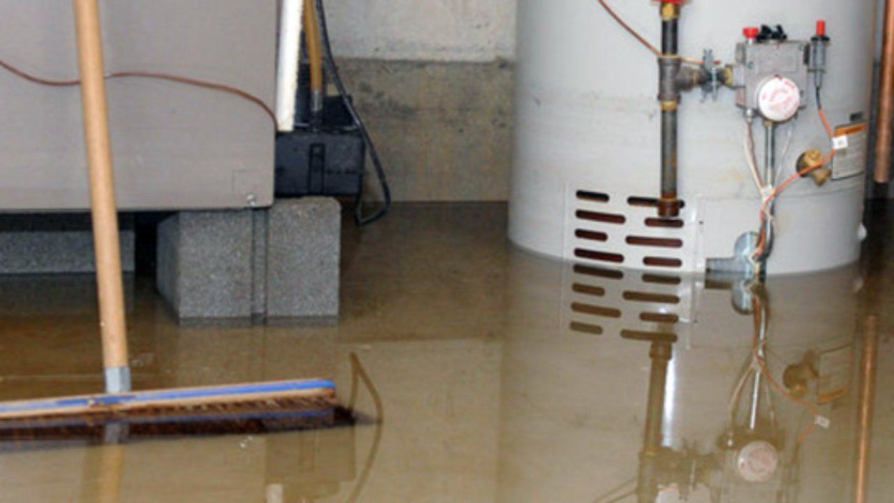A flooded basement with a water heater and a broom.