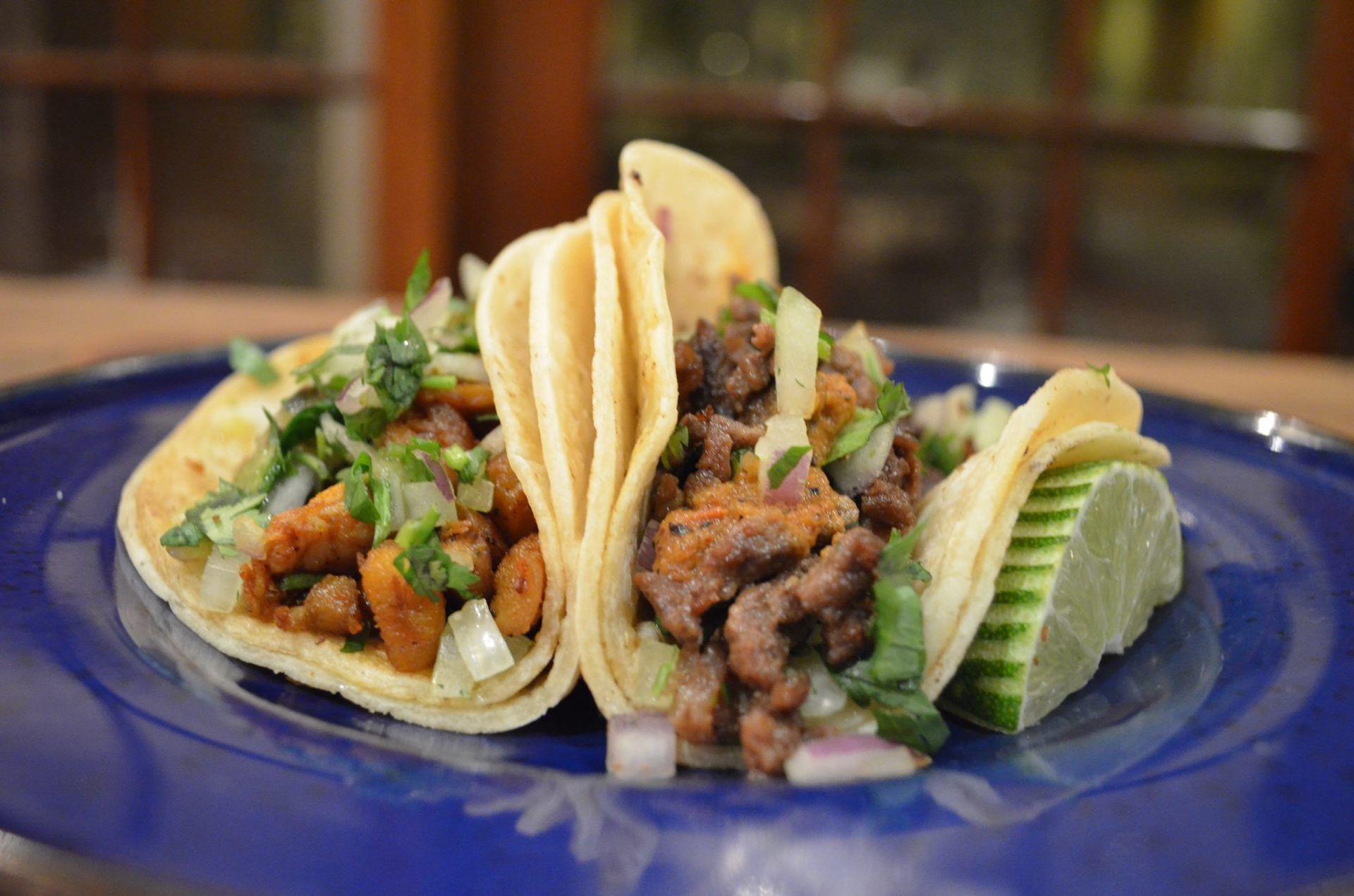 Three tacos are on a blue plate on a table.