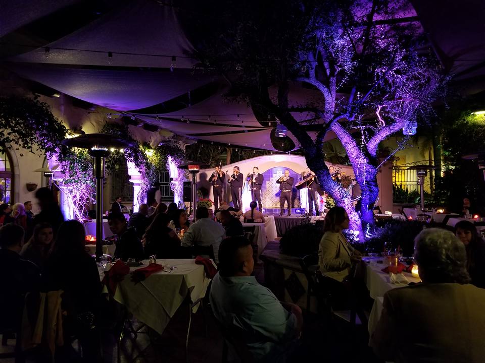 A group of people are sitting at tables in a restaurant watching a band perform on stage.
