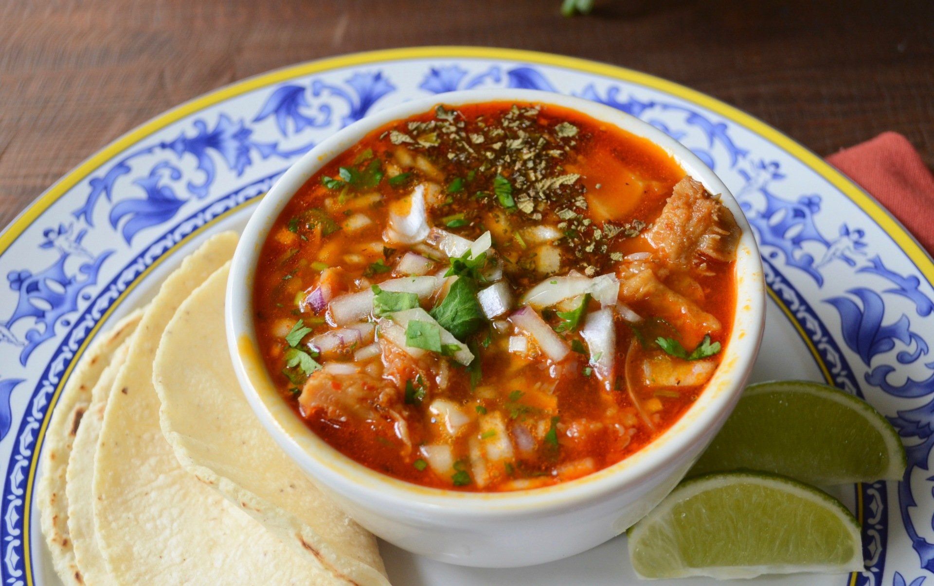 A bowl of soup is on a plate with tortilla chips and lime wedges.