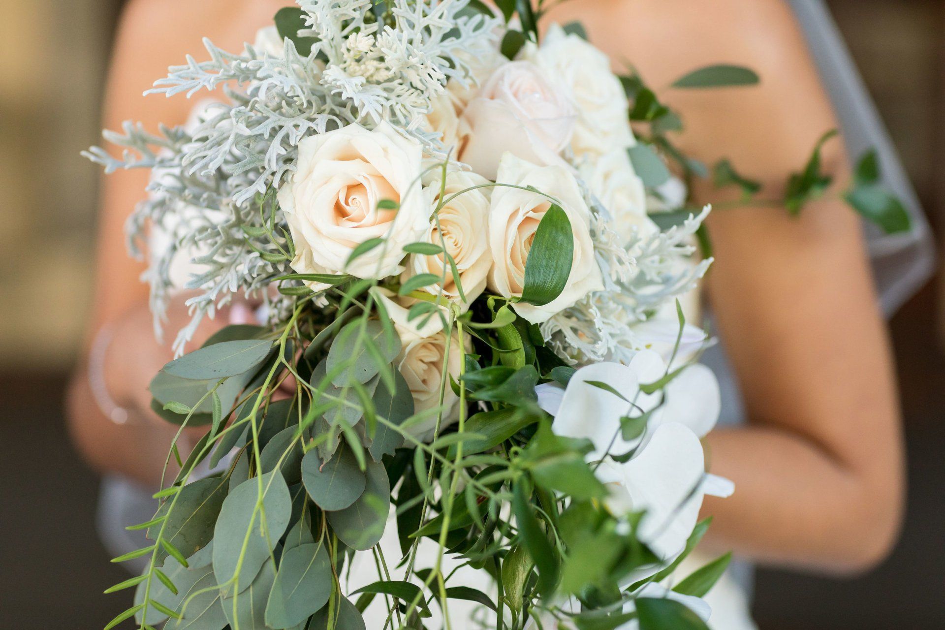 A bride is holding a bouquet of white roses and greenery.