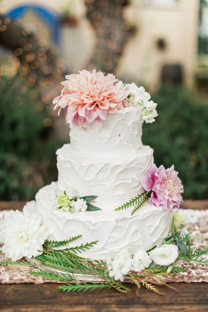 A white wedding cake with pink and white flowers on top is sitting on a wooden table.