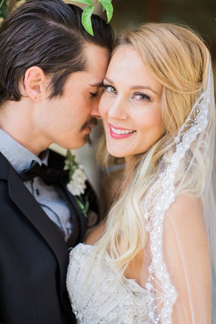 A bride and groom are posing for a picture and the bride is wearing a veil.