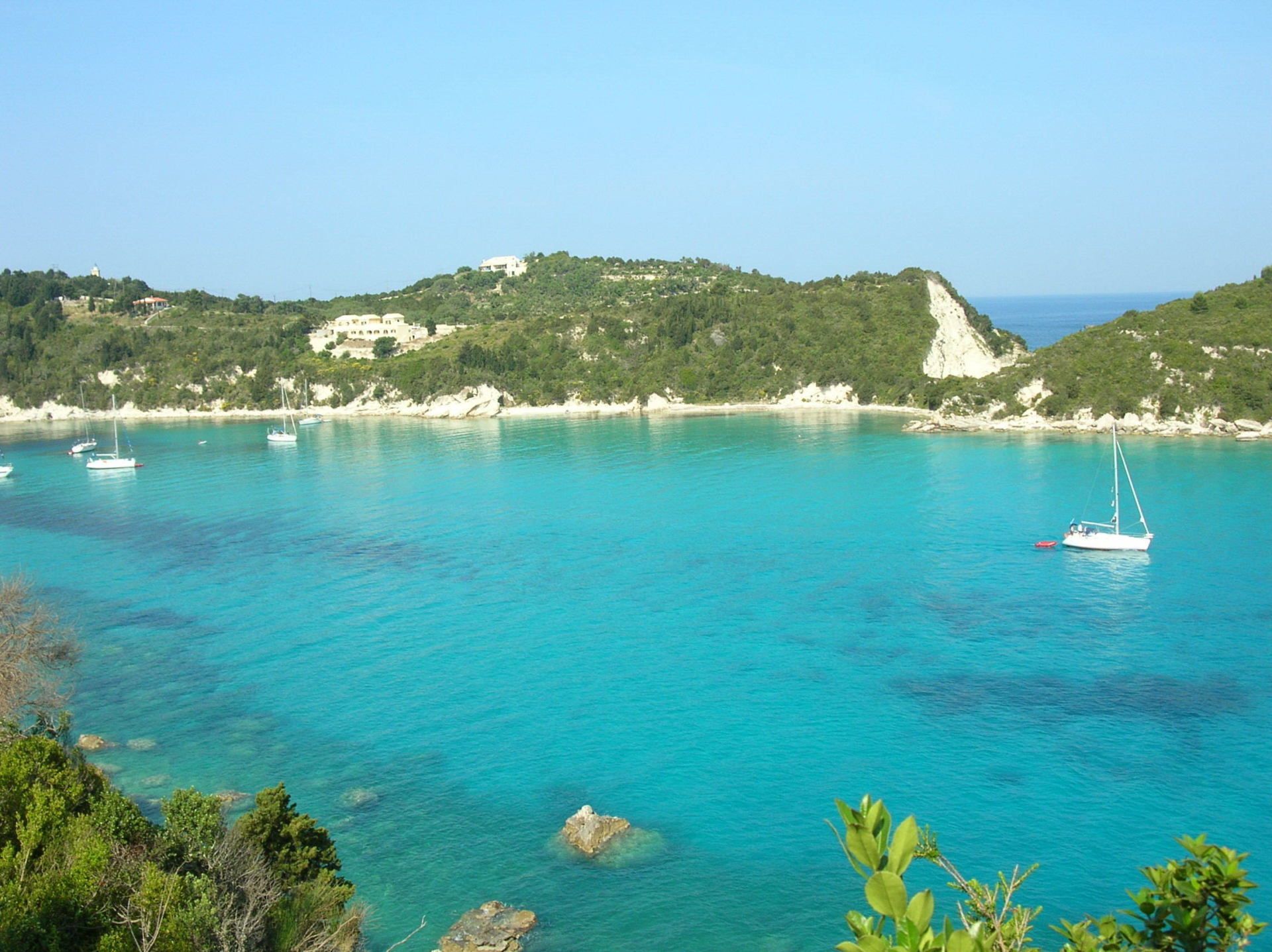 Turquoise bay with rocky green shoreline and two small white sailboats under a clear sky